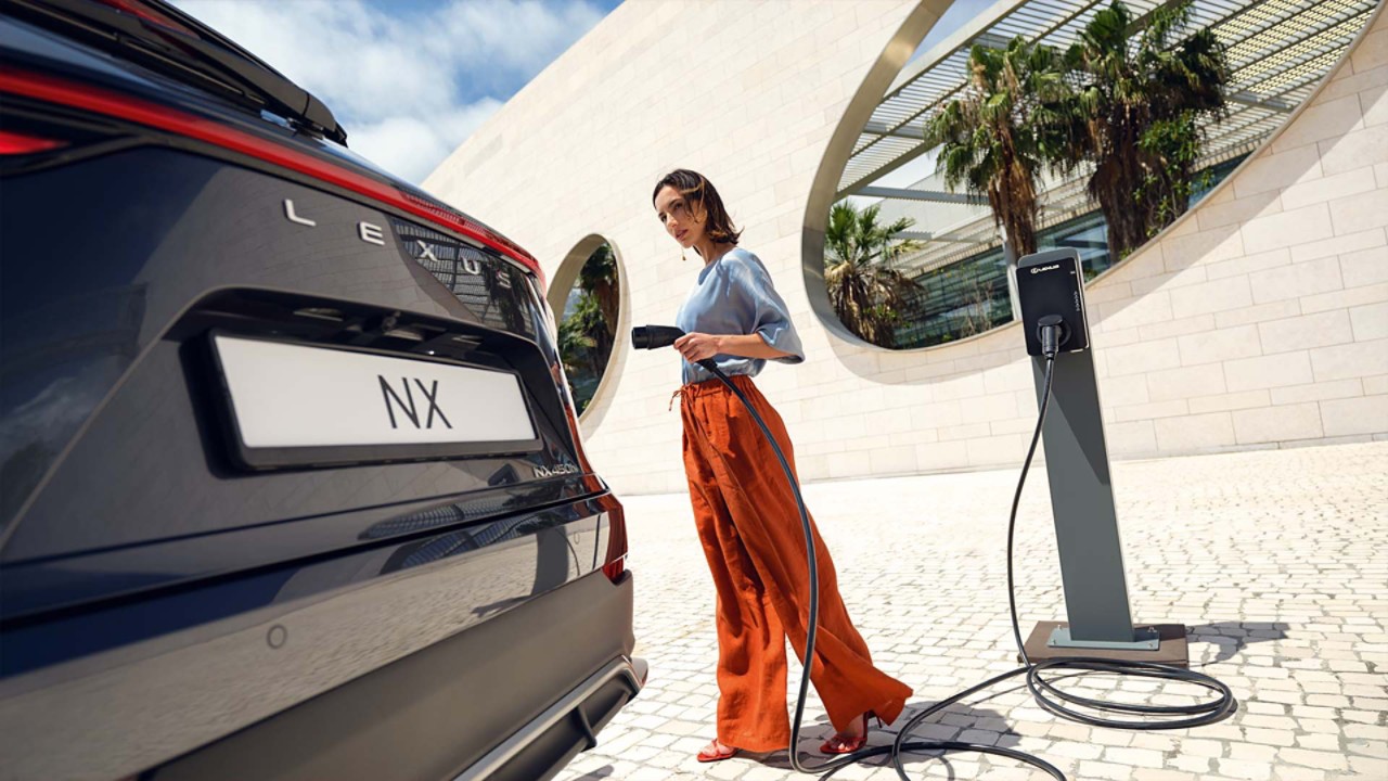 A person approaching a parked Lexus NX with a charger.